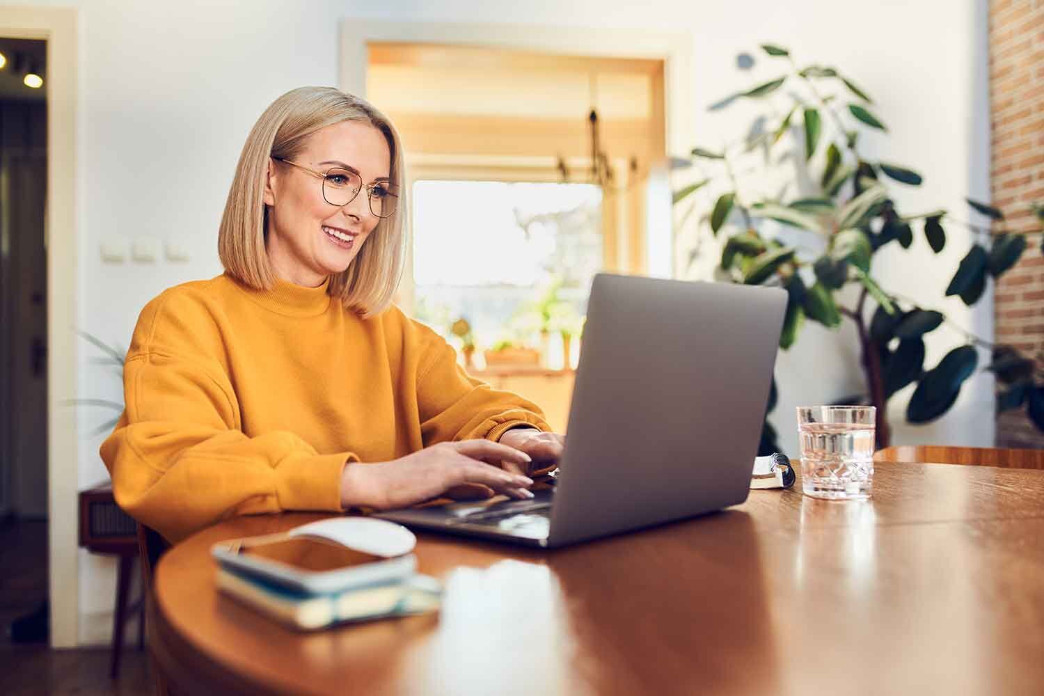 eine Frau sitzt an einem Tisch mit einem Laptop vor orangenem Hintergrund